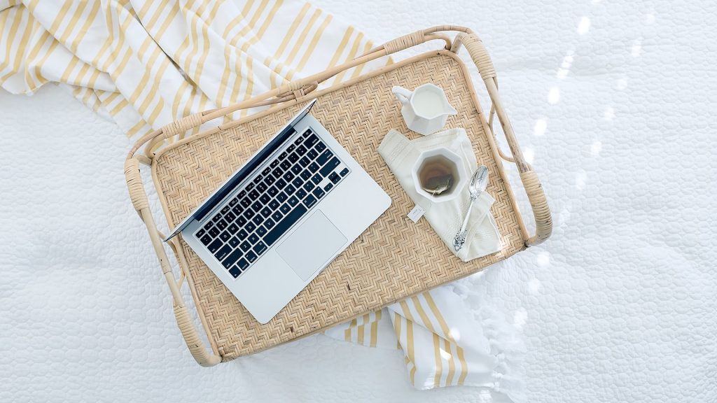 Laptop on a tray with tea and cream