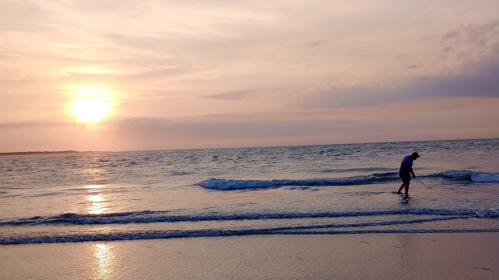 A man shelling in shallow beach water during sunrise